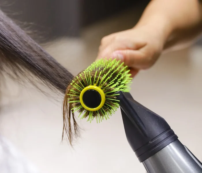 Profissional modela os cabelos com escova redonda e secador